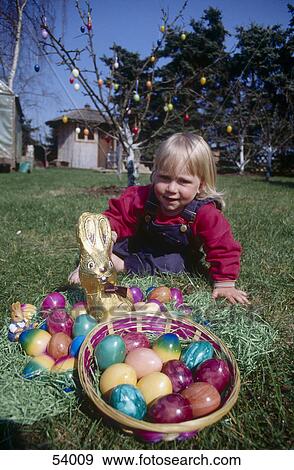 Stock Photo - Girl sitting with Easter eggs in lawn . Fotosearch