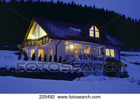 Stock Image - House on snowcovered landscape lit up at dusk . Fotosearch