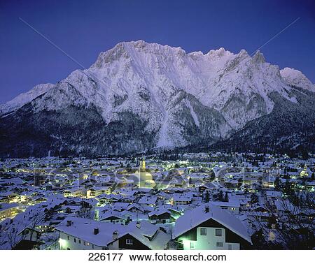 Stock Photo - Houses in town lit at dusk in front of mountain range, Karwendel Mountains, Bavaria, Germany . Fotosearch