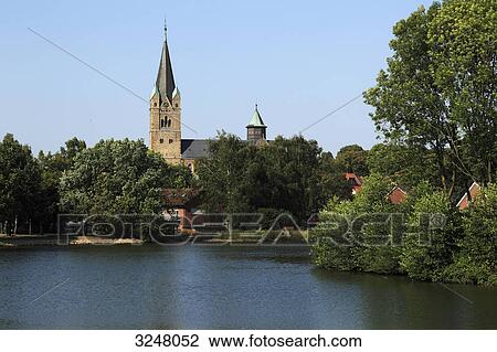 Stock Image - Lake in Ankum, view of the steeple of Saint Nicholas Church, Germany . Fotosearch