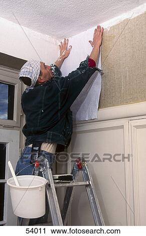 Stock Image - Man pasting wallpaper on wall . Fotosearch