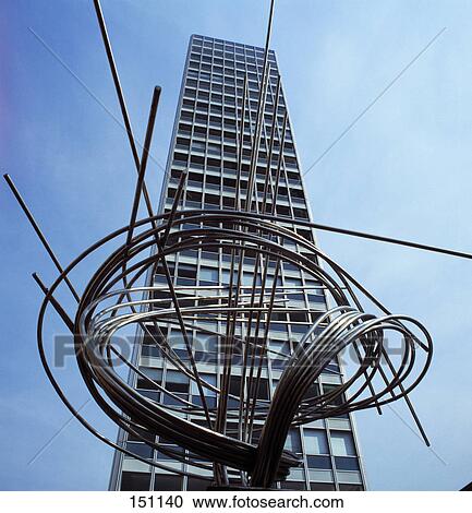 Stock Image - Metal sculpture in front of high rise building against blue sky, Germany . Fotosearch