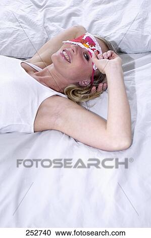Stock Image - Portrait of young woman lying on bed and smiling . Fotosearch