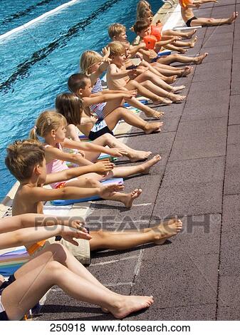 Stock Photo - Side profile of children sitting in row at poolside, Egelsbach, Hesse, Germany . Fotosearch