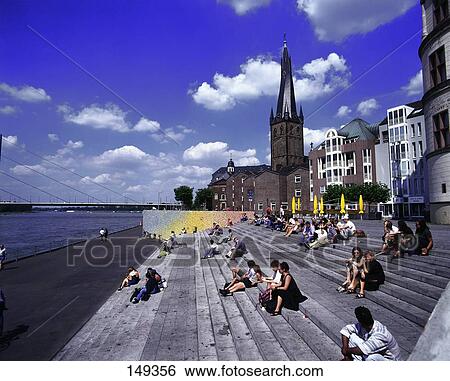 Stock Photograph - Tourists sitting on steps at coast, Lambertuskirche, Düsseldorf, North Rhine Westphalia, Germany . Fotosearch