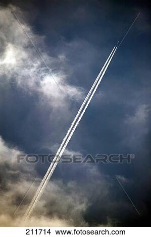 Picture - Vapour trail behind clouds on sunset sky . Fotosearch