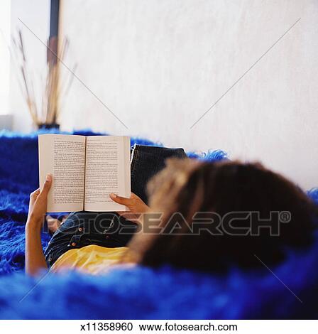 A Young Woman Lying On A Couch And Reading A Book Stock Image