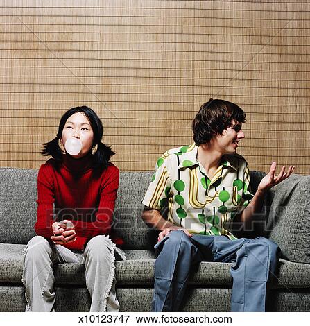 View Of A Woman Sitting On A Couch Blowing A Bubble With A Man