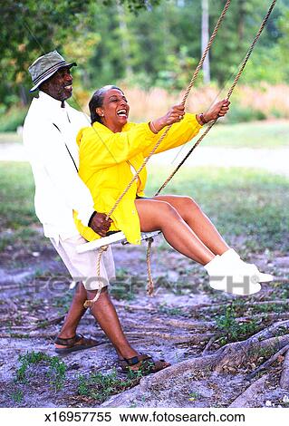 Side Profile Of An Elderly Man Pushing An Elderly Woman On A Swing Stock Photography