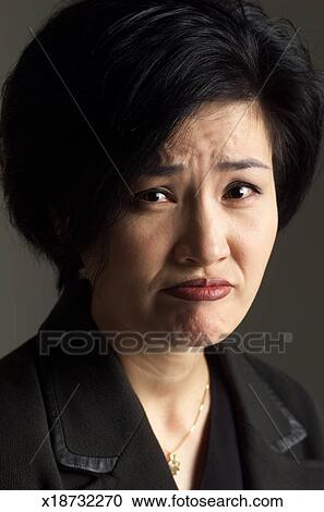 An Asian Woman Wearing A Dark Suit Has Short Hair And Is Frowning