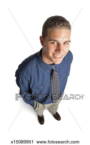 Handsome Young Man With Short Curly Blonde Hair And Blue Eyes Wearing A Blue Shirt And Tie Tan Pants And Brown Shoes Looks Up To The Camera And Smiles