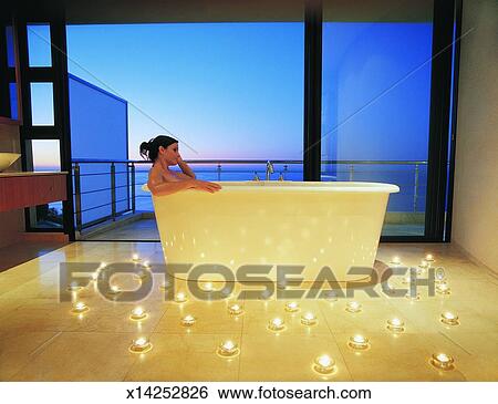 Stock Image - Woman Relaxing in Luxury Bath Surrounded By Candles Against Open View of the Sea. Fotosearch - Search Stock Photography, Poster Photos, Pictures, and Photo Clip Art