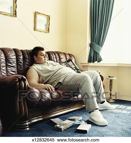 Stock Image Of Young Man Lies Slouched On A Sofa Watching Videos And Stock Image Young Man Lies Slouched On A Sofa Watching Videos And Holding Packet