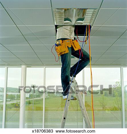 Man On Step Ladder Working Through Gap In Ceiling Low Section