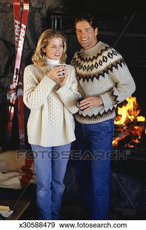 Couple In Ski Lodge Standing By Fireplace Portrait Stock Photo
