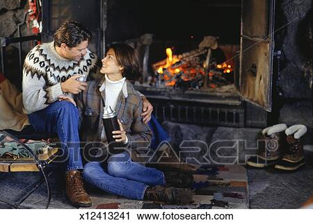 Couple Sitting In Ski Lodge By Fireplace Woman Holding Insulated