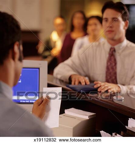 Young Man Standing At Counter In Bank Teller Checking Receipt