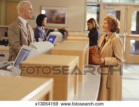 Woman Talking With Bank Teller At Reception Desk Side View Stock