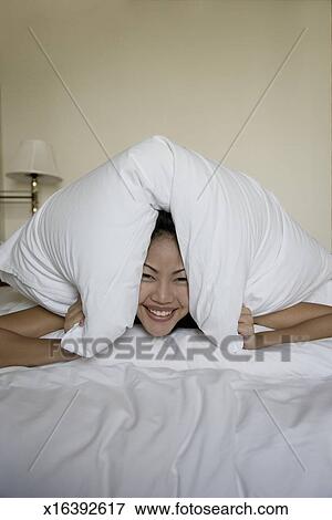 Young Woman Lying In Bed Hiding Under Pillow Smiling Portrait