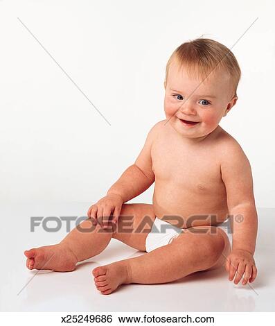 A Young Happy Smiling Baby With Blonde Hair And Blue Eyes Sits In