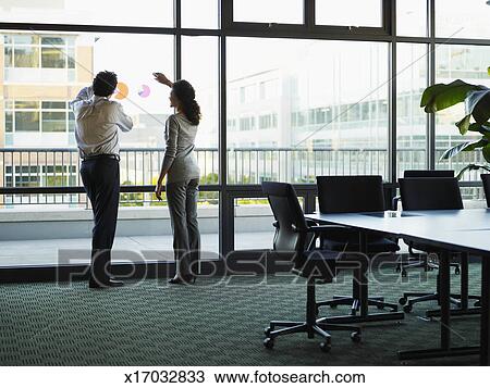 Two Business People Looking Out Windows In Conference Room Stock Image