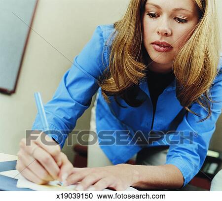 Businesswoman Bending Over At Her Desk And Writing On A Piece Of