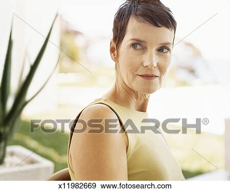 Mature Woman With Short Hair Sits In A Sleeveless Dress In A