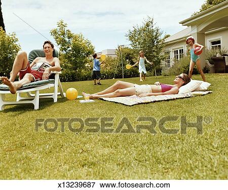 Three Children Play With Balls In A Garden While Their Parents Are