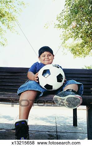 Boy Sits On A Park Bench Holding A Football Stock Photo