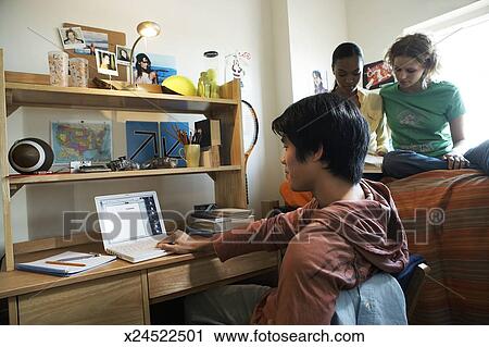 Young Man And Two Young Women Studying In Bedroom Women Sitting On Bed Stock Image
