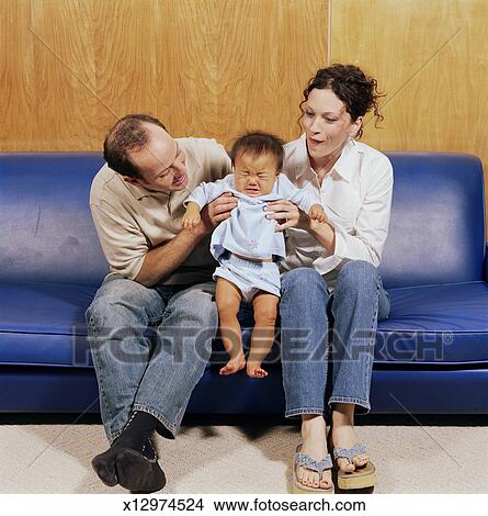 Couple on couch holding crying adopted baby girl (9-12 Couple on couch holding crying adopted baby girl (9-12