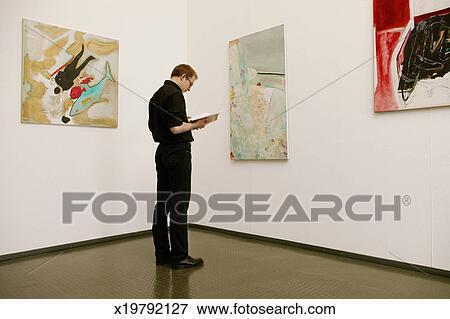 Man Standing In Front Of Painting Looking Down At Book Stock