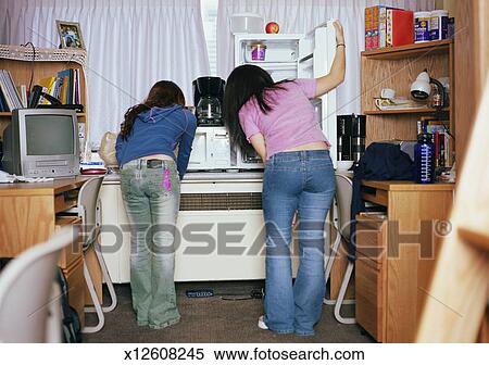 Two Young Women Looking In Refrigerator In Dorm Room Rear