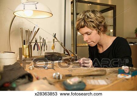 Woman At Work Bench In Jewellers Using Device On Jewellery Piece