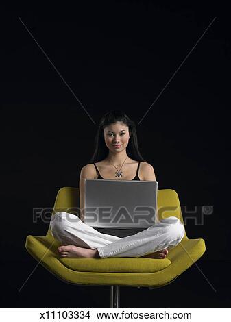 Teenage Girl 16 18 Sitting Cross Legged On Chair Using Laptop