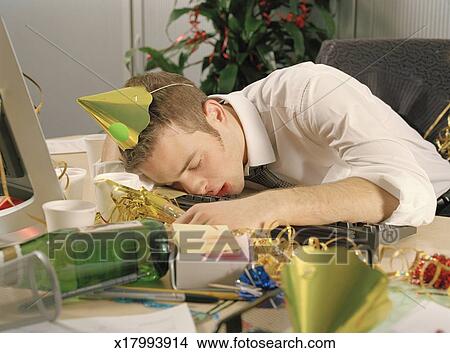 Young Man Asleep At Desk Surrounded By Remnants Of Office Party