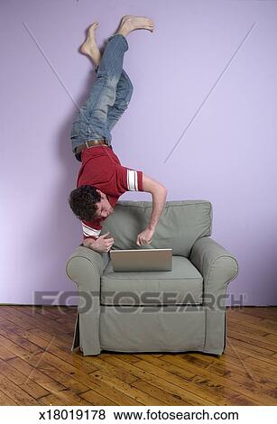 Young Man Upside Down On Chair Using Laptop Stock Photo