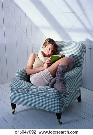 Young Woman Curled Up In Chair Reading Book Stock Image