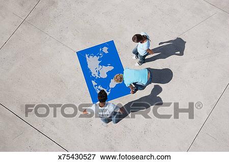 Aerial View Of Three People Looking At World Map Puzzle Outdoors