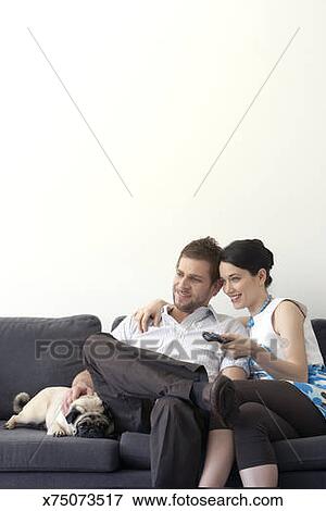 Young Couple Sitting On Couch With Dog Watching Television Stock