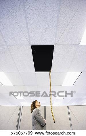 Female Office Worker Looking Up At Rope Dangling From Hole