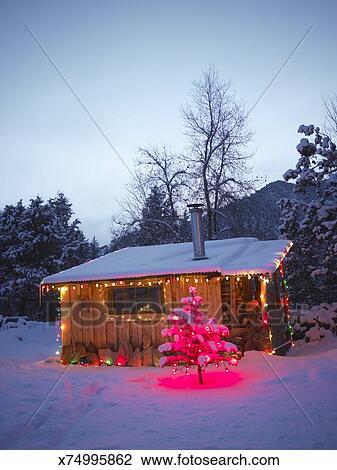Log Cabin Decorated With Christmas Lights In Snow At Dusk Stock