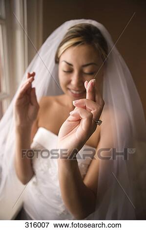 Stock Photo - Bride standing with eyes closed and fingers crossed. Fotosearch