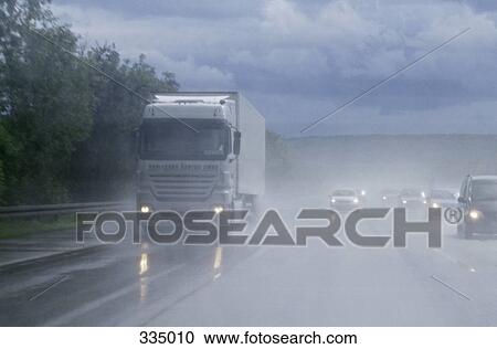 Stock Image - Semi truck and cars traveling on highway in the rain. Fotosearch