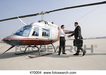Businessmen shaking hands by a helicopter View Large Photo Image Picture - Businessmen shaking hands by a helicopter. Fotosearch