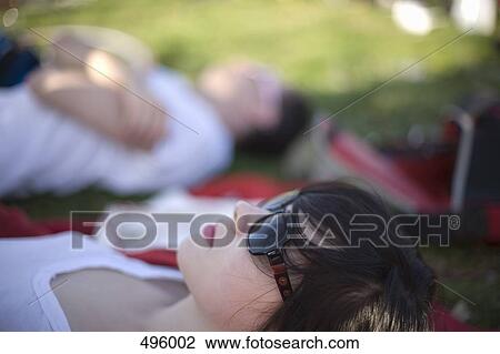 Stock Image - A young woman lying down in a park. Fotosearch