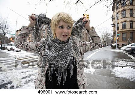 A young woman putting a scarf on whilst standing on a street corner View Large Photo Image Stock Image - A young woman putting a scarf on whilst standing on a street corner. Fotosearch
