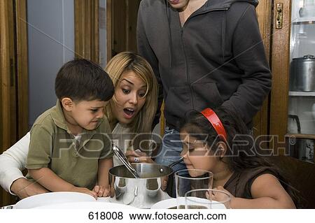 Stock Photo - A family sitting at a dining table and looking shocked. Fotosearch