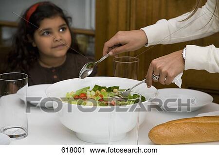A girl sitting at a table and a woman serving salad View Large Photo Image Stock Image - A girl sitting at a table and a woman serving salad. Fotosearch