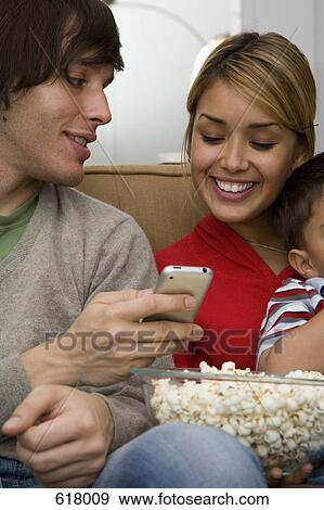 A man and woman sitting on the sofa with a bowl of popcorn and a remote control View Large Photo Image Stock Photo - A man and woman sitting on the sofa with a bowl of popcorn and a remote control. Fotosearch